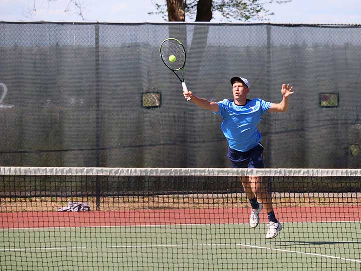 Men's tennis player striking the ball over the net