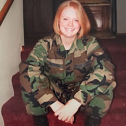 A young Katlin Gamche, seated and facing the camera. She's wearing full camouflage, likely taken during her time in the Air Force.
