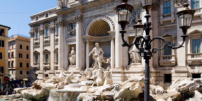 The famous trevi fountain in Rome showing an an old and interesting street lamp in the foreground.