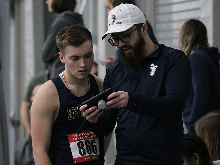 men's track and field teammate looking at a smartphone with coach.