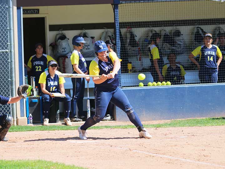 Softball player hitting the ball mid swing with team in view