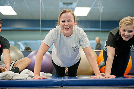 Young women do pushups next to one another on an exercise mat.