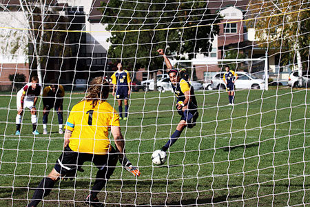 Soccer goalie getting ready to block the ball. Soccer player is kicking the ball towards the goal.